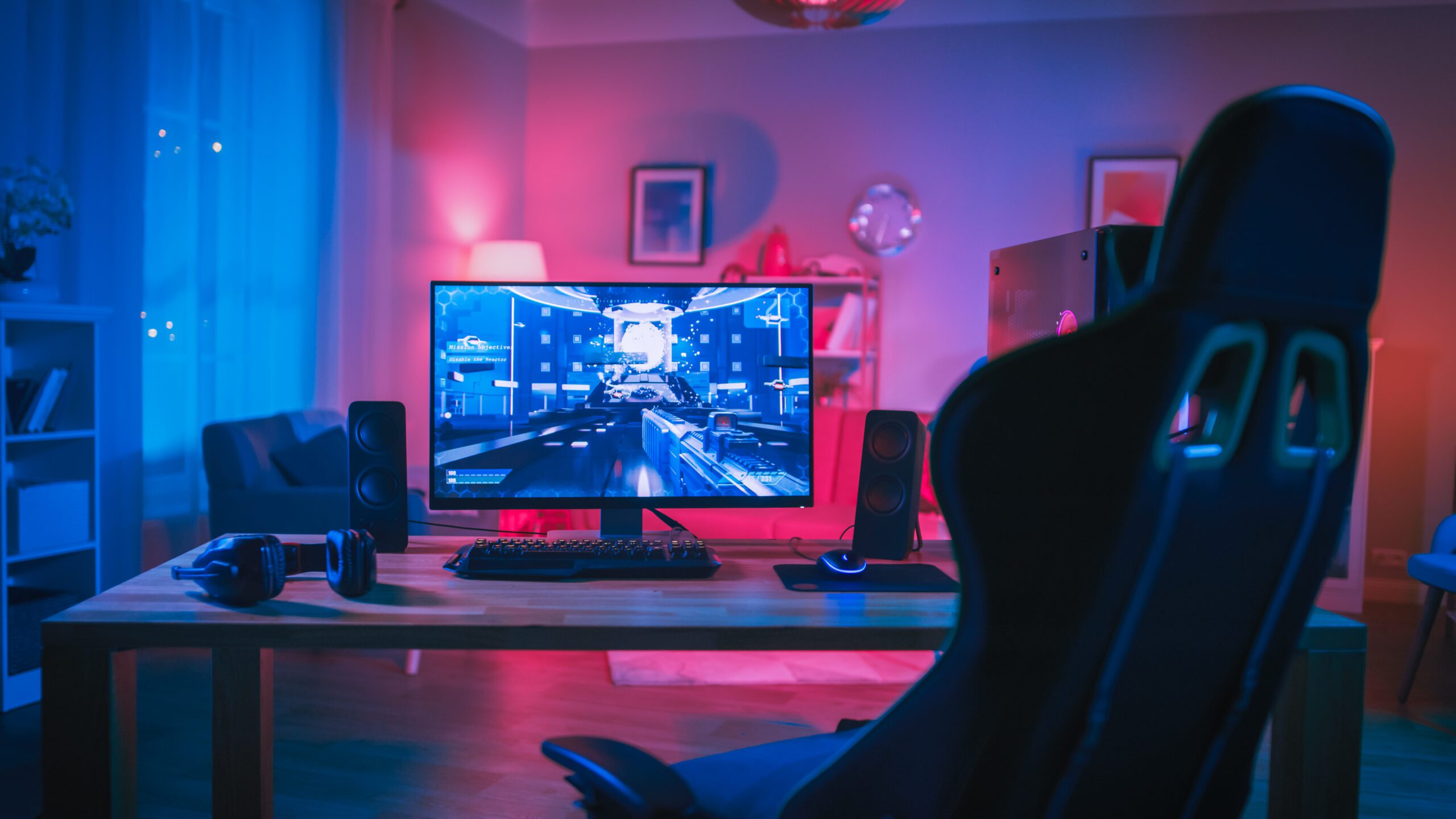 Powerful Personal Computer Gamer Rig with First-Person Shooter Game on Screen. Monitor Stands on the Table at Home. Cozy Room with Modern Design is Lit with Pink Neon Light.